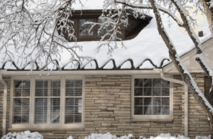 House roof with thick ice dams and long icicles forming along the eaves after heavy snowfall