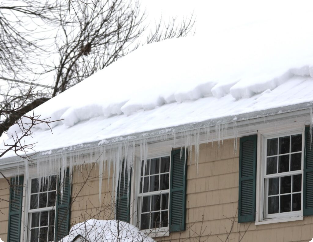 Snow-covered roof with ice dam and icicles hanging over the edge of a residential home