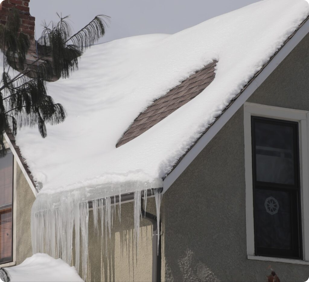 House roof with thick ice dams and long icicles forming along the eaves after heavy snowfall