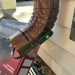 Copper pipe wrapped with heat tape and a black sensor device with a green LED attached