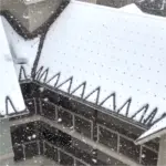 Snow-covered roof edge with metal bird spikes along the eaves.
