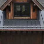 Wooden dormer window on a rustic house, with a dark metal roof and exposed timber siding above a wooden wall.