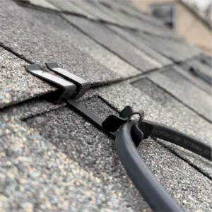 Close-up of a black cable secured along asphalt shingle roof with two plastic clips