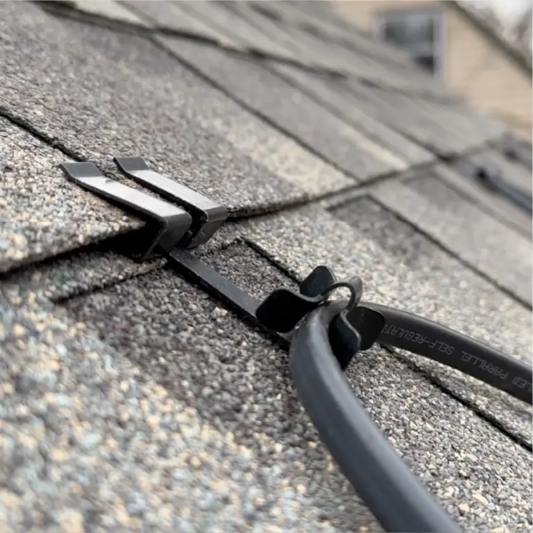 Close-up of a black cable secured along asphalt shingle roof with two plastic clips