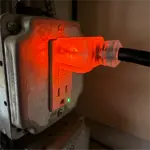 Industrial electrical outlet with orange glow from the connected plug and a green indicator light